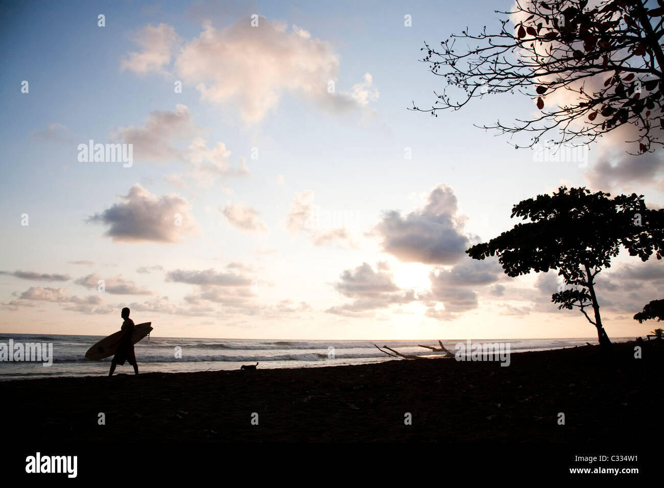 Eine Silhouette Bild eines Mannes geht unten am Strand, gefolgt von einem Hund den Sonnenuntergang hinter ihnen. Stockfoto