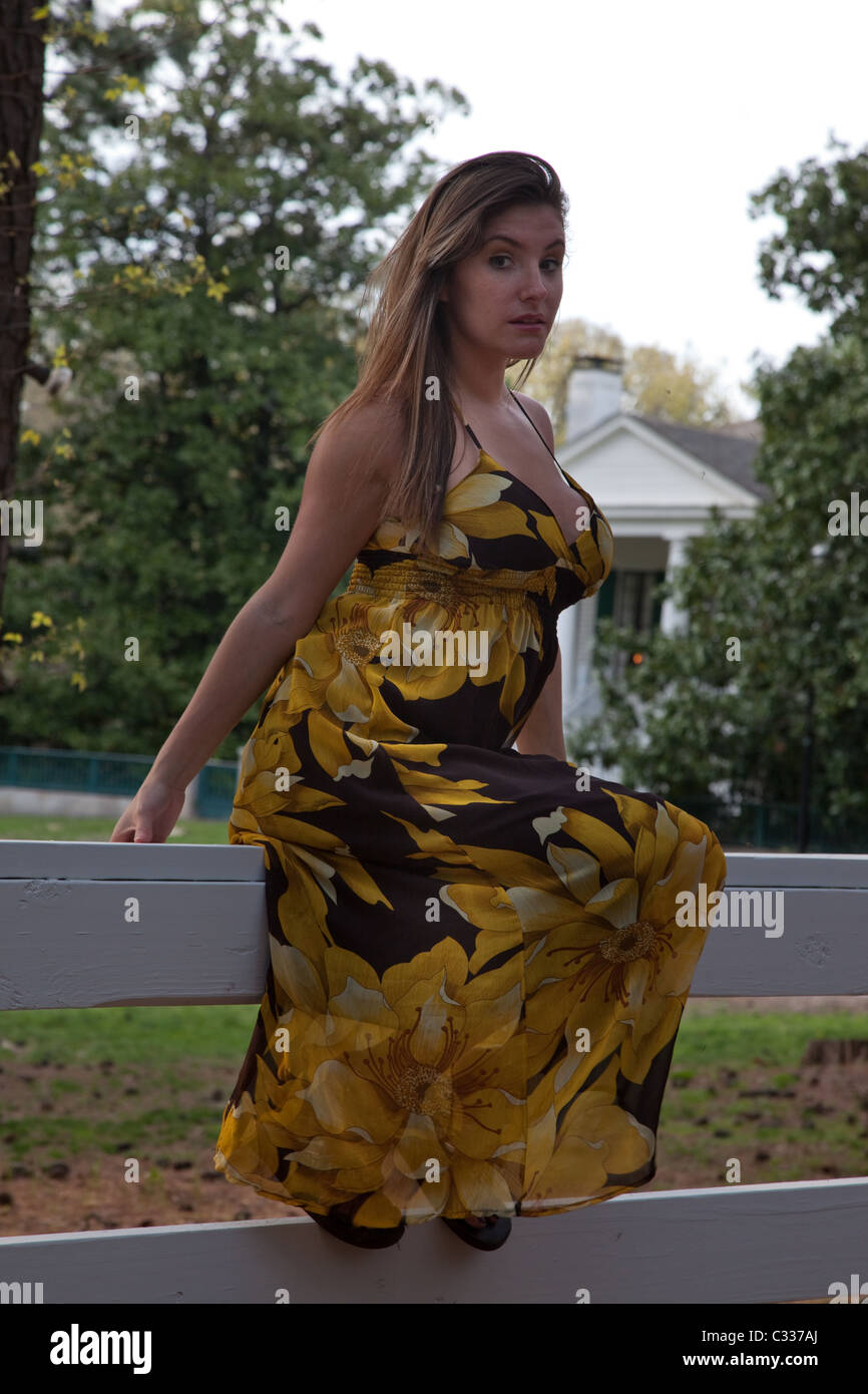 Schöne weiße Frau trägt ein gelbe-schwarze Kleid, draußen sitzen auf einem weißen Zaun Stockfoto