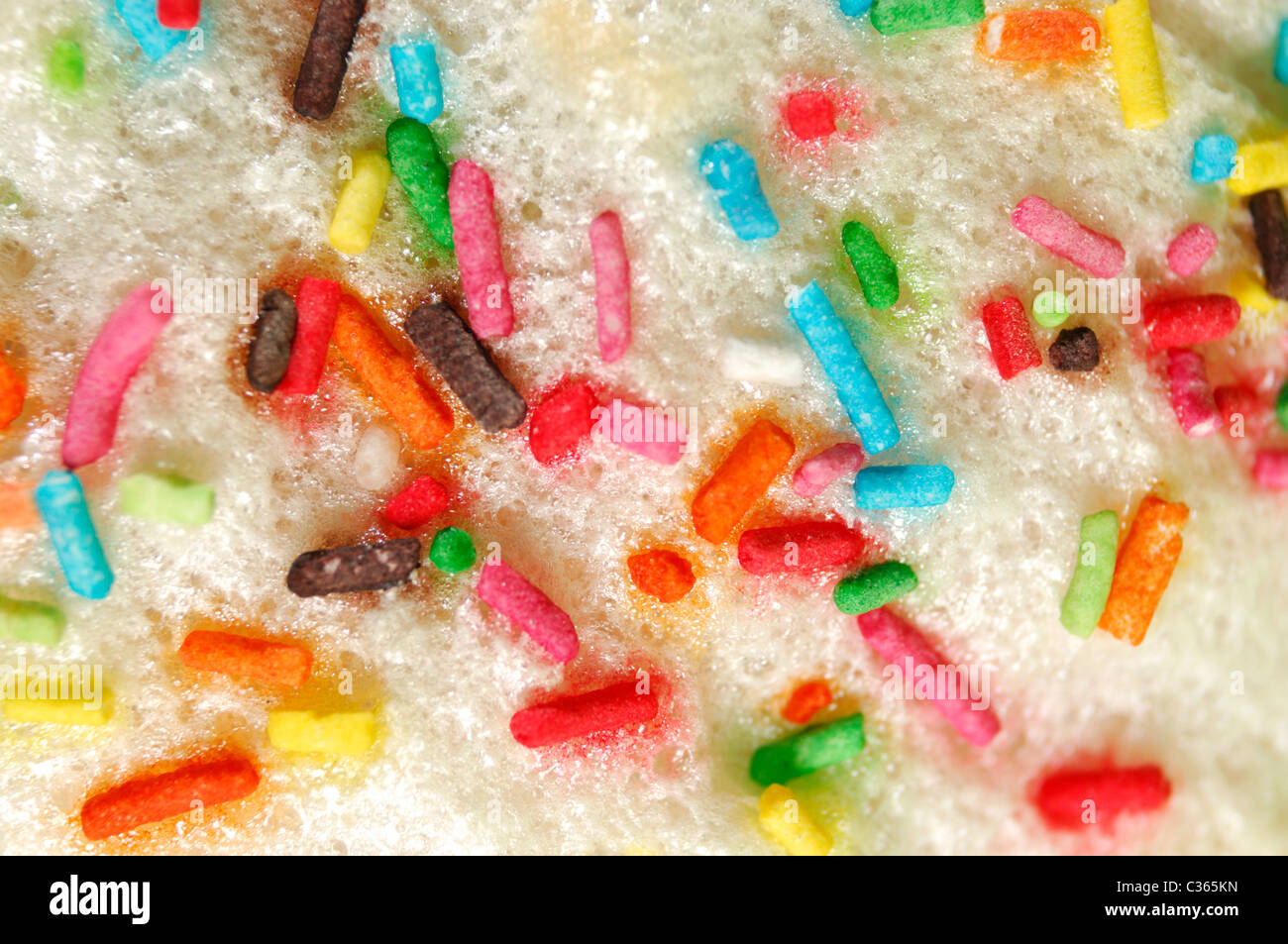 Nahaufnahme von einem Osterkuchen mit weißem Zuckerguss gesprenkelt mit farbigen Süßigkeiten Streusel künstlerische Makro Hintergrundtextur Stockfoto
