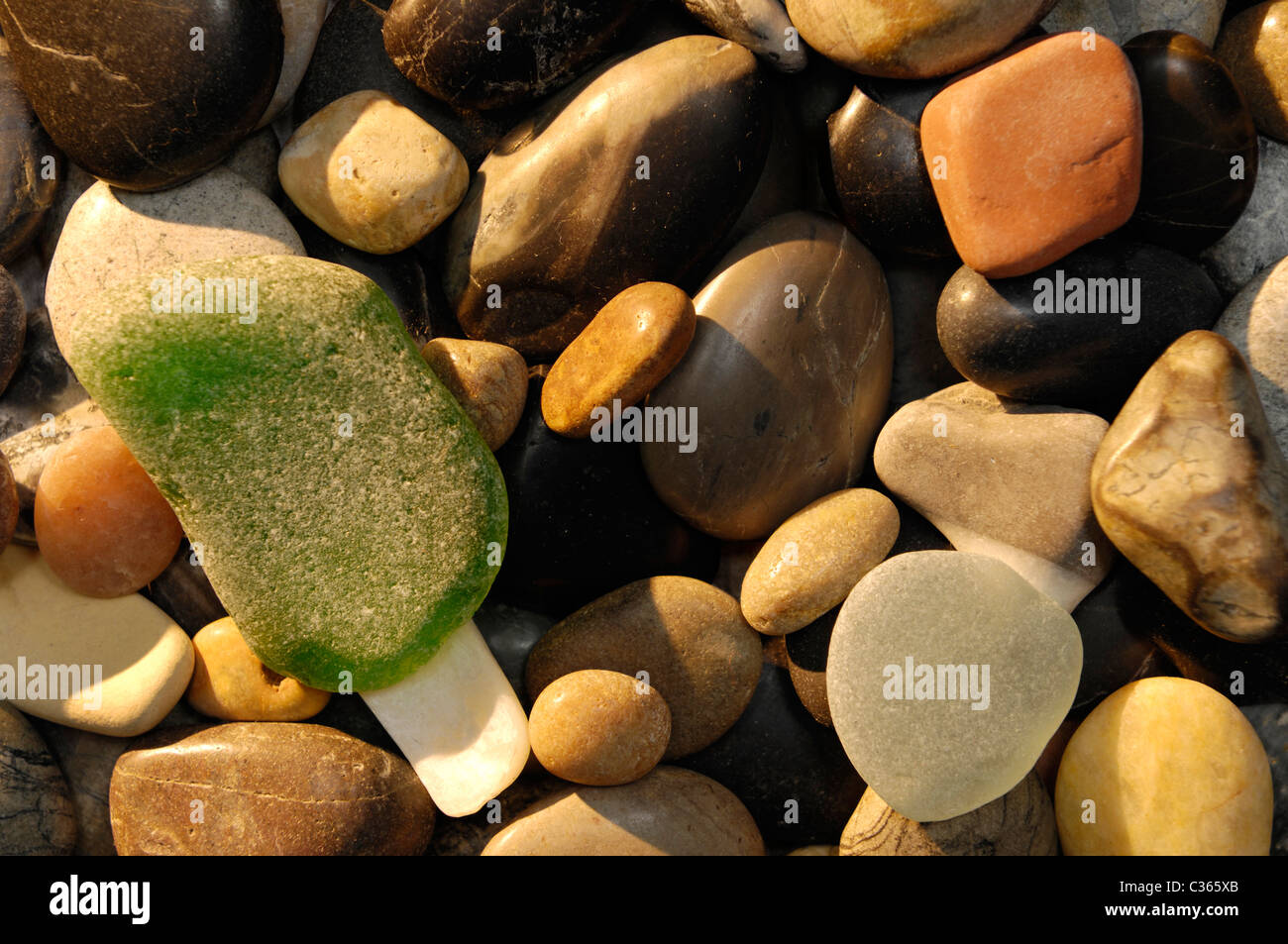 Abgerundeten Steinen auf einem Kiesstrand in Morgen Sonnenlicht abstrakte Closeup Hintergrundtextur Stockfoto