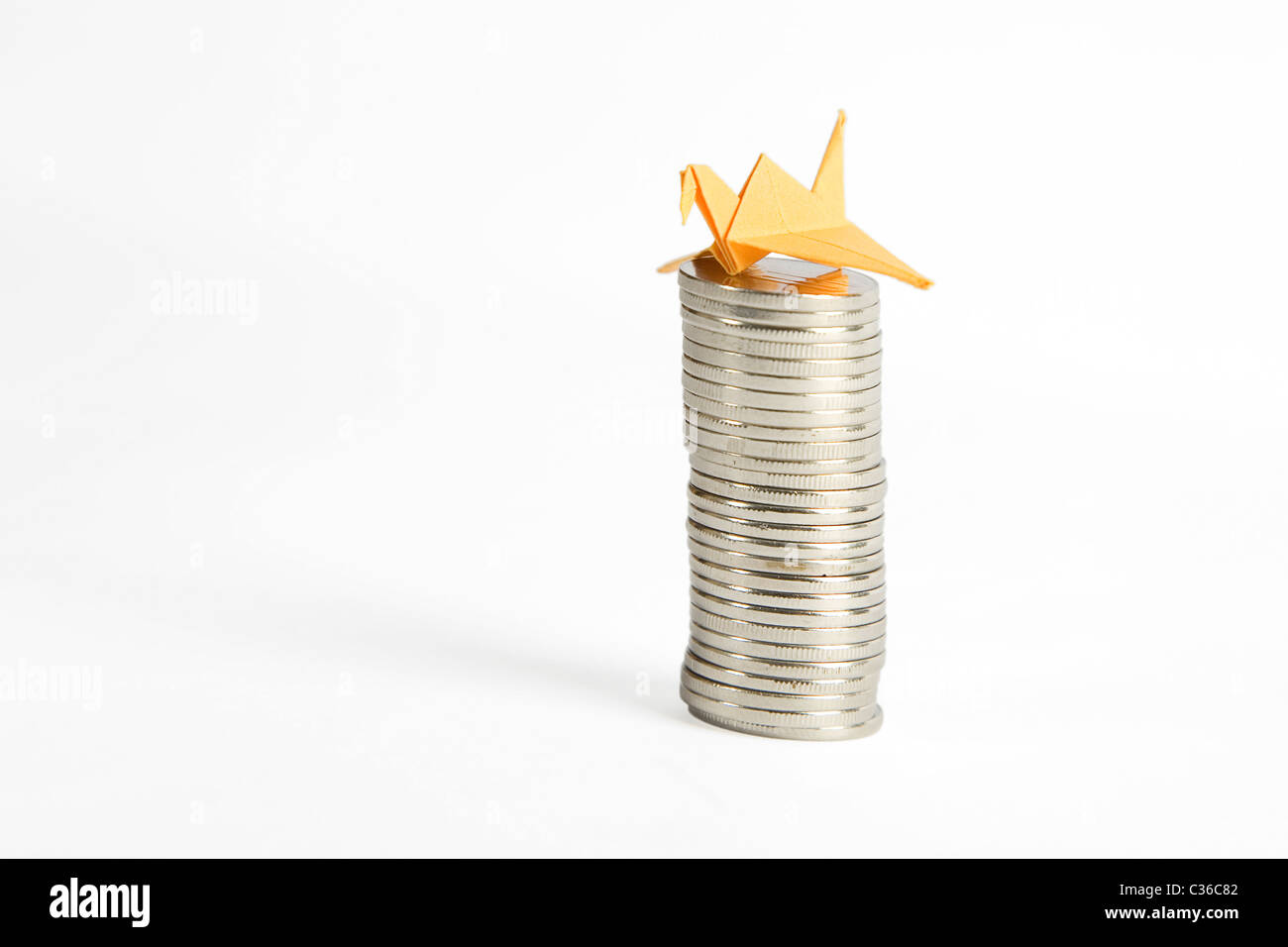 Stapel von Silbermünzen und gelbe Origami Vogel isoliert auf weißem Hintergrund Stockfoto