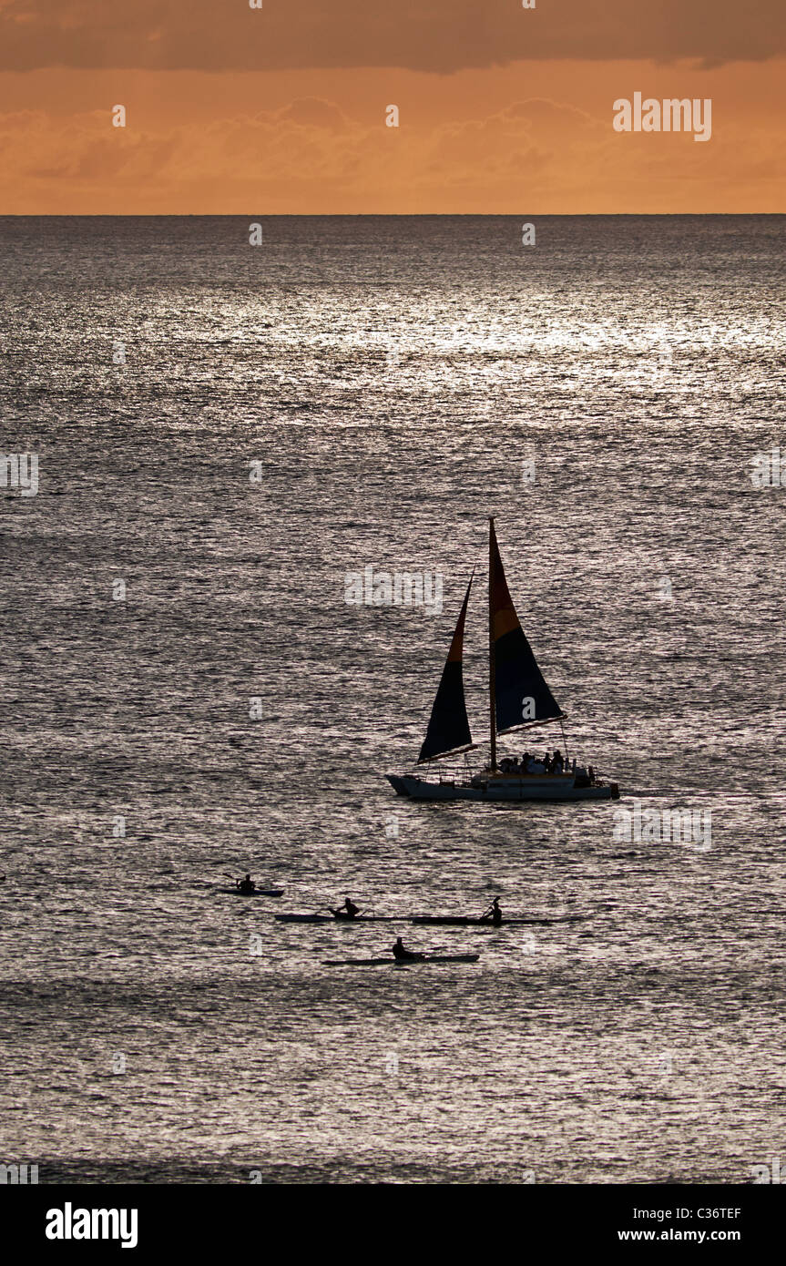 Eine erhöhte Ansicht eine Silhouette Segelboot und Kajaks in den Gewässern von Waikiki, Honolulu, Hawaii. Stockfoto