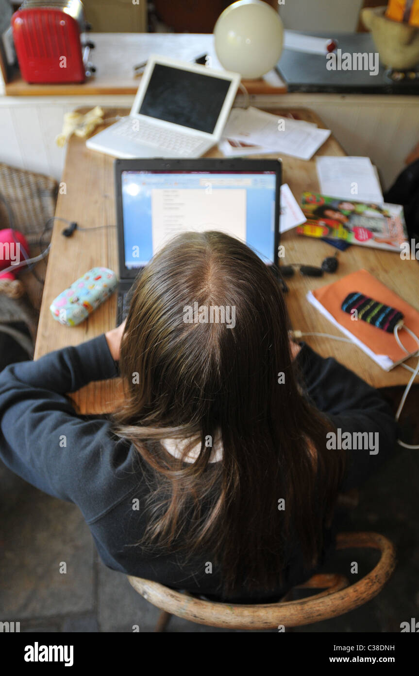 Ein 13 Jahres altes Mädchen macht ihre Hausaufgaben auf einem Computer an einem unordentlichen Küchentisch Stockfoto