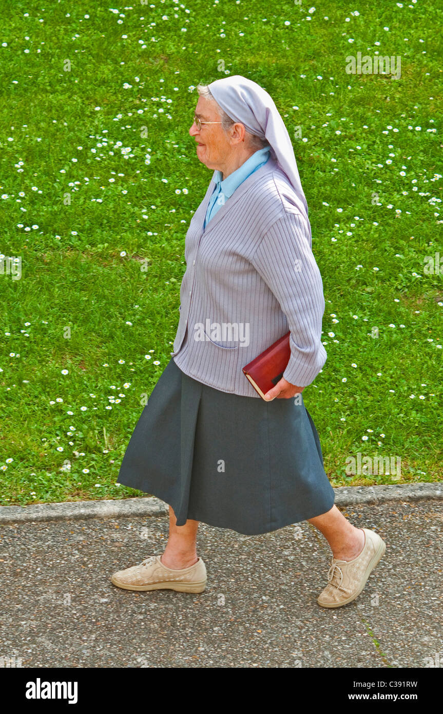 Ältere Nonne zu Fuß entlang der Fahrbahn - Frankreich. Stockfoto