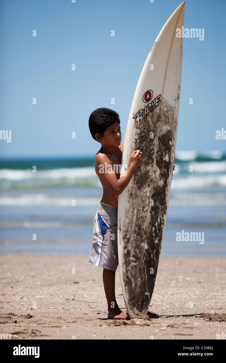 Ein kleiner Junge hält einen überdimensionierten Surfbrett an einem Strand in Costa Rica Stockfoto