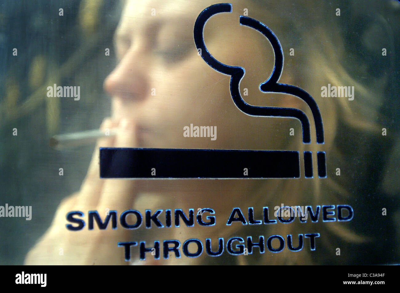 Eine junge Frau mit einer Zigarette Pause auf ein Zeichen "Rauchen erlaubt" Stockfoto