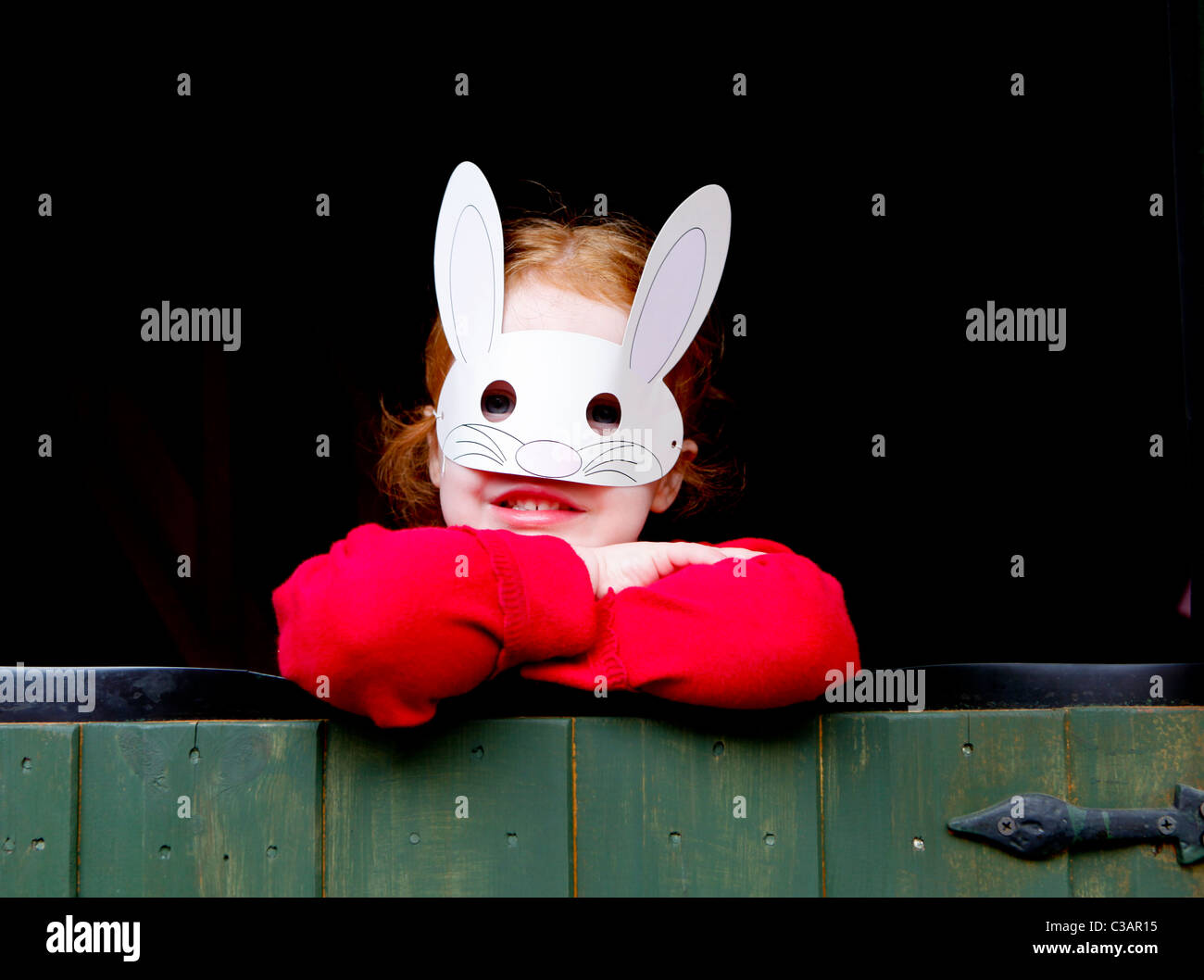 Ein vier Jahre altes Mädchen mit Ingwer Haar eine Ostereiersuche in einem Garten mit einer Kaninchen-Maske zu tun. Stockfoto