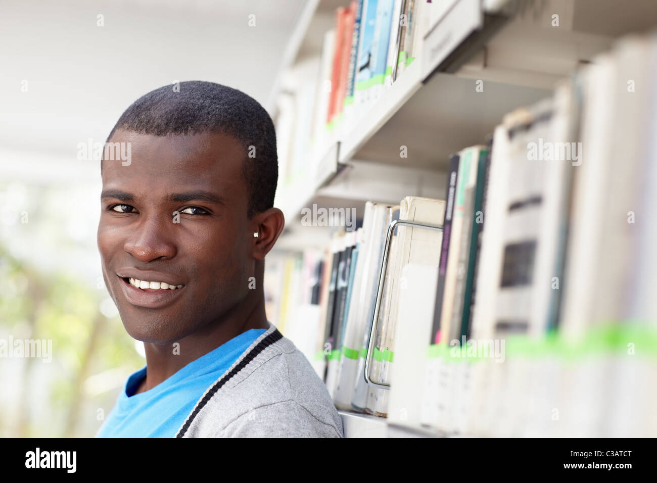 junge afrikanische amerikanische College-Studentin in Bibliothek, Blick in die Kamera in der Nähe von Regal Stockfoto