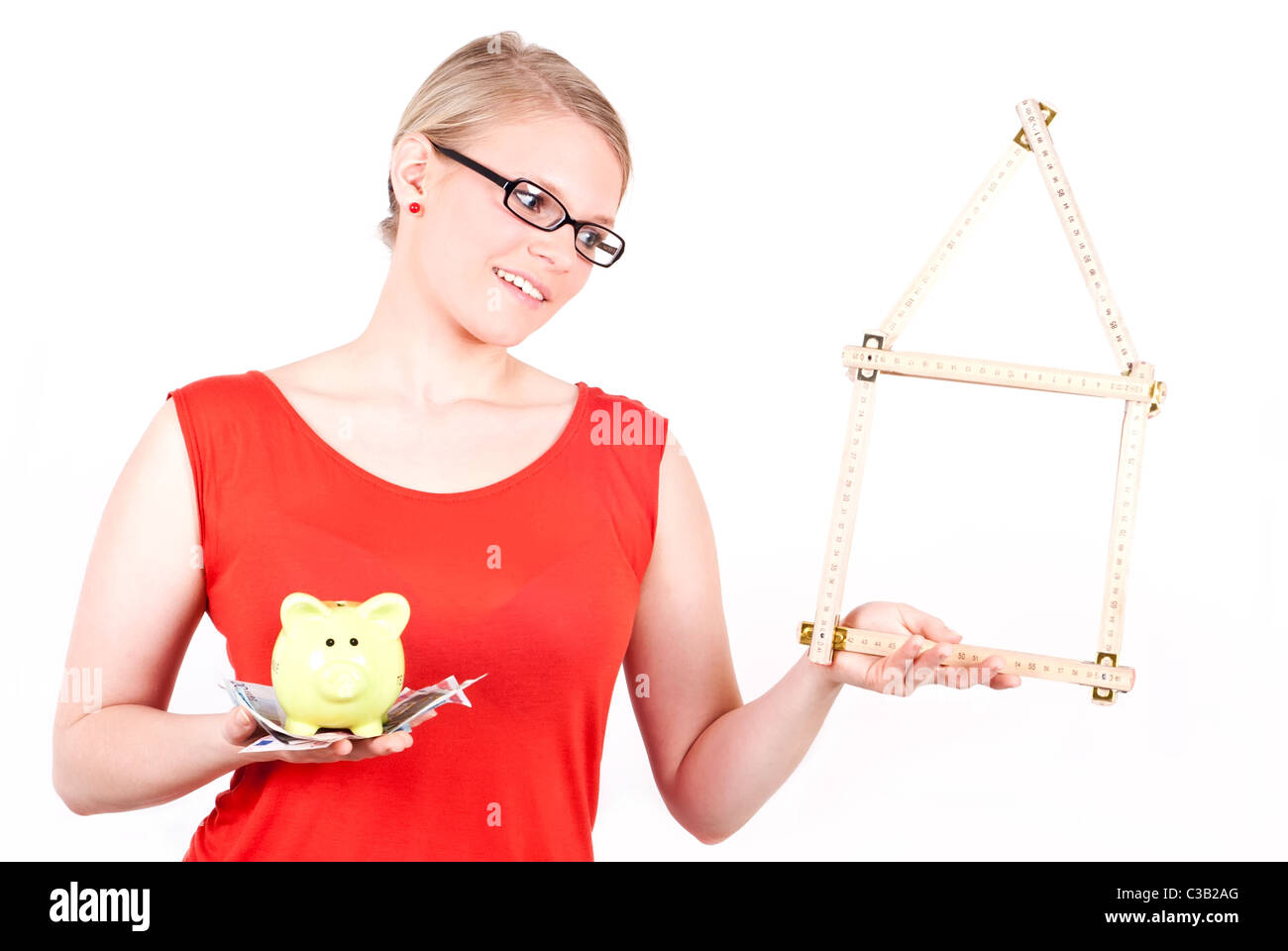junge Frau mit klappbarem Regel als Haus-Symbol und Sparschwein vor weißem Hintergrund Stockfoto