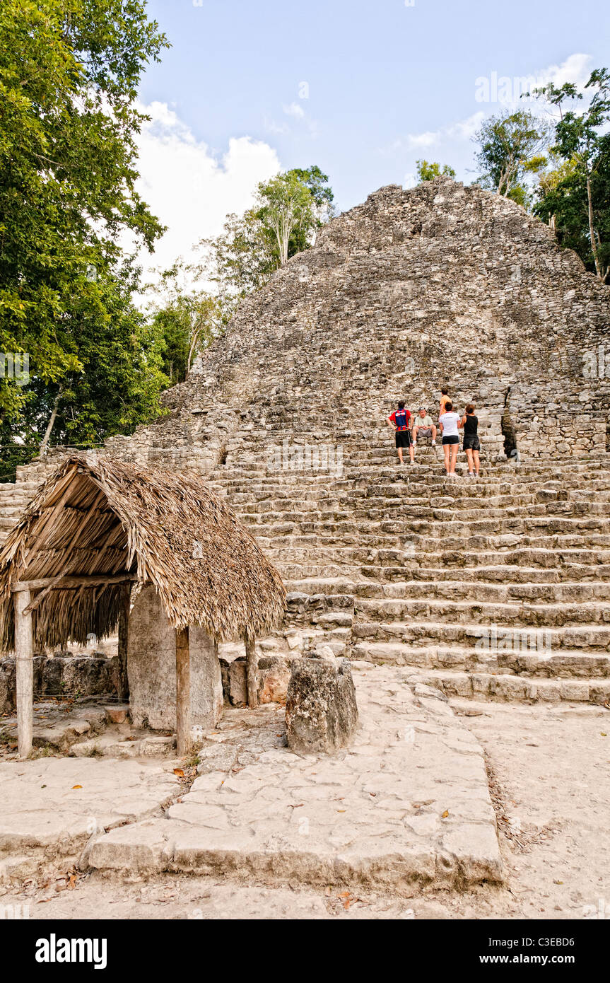 Coba Maya-Stätte La Iglesia Pyramide Mexiko // COBA, Quintana Roo, Mexiko - Touristen klettern die 120 Stufen der Tempelstruktur, bekannt als La Iglesia (die Kirche), die zweithöchste Pyramide an der Maya-archäologischen Stätte von Coba. Das kleine Gebäude mit dem Strohdach im Vordergrund wurde als Stela 11 bezeichnet, eines der bedeutendsten Inschriften des Ortes, das an den Herrscher Xaman K'awiil erinnert. La Iglesia ist etwa 24 Meter 79 hoch und wurde während der frühen Klassik (ca. 300–600 n. Chr.) als Teil der Cobá-Gruppe, dem ältesten Zeremonialgebiet an diesem Ort, erbaut. Coba Stockfoto