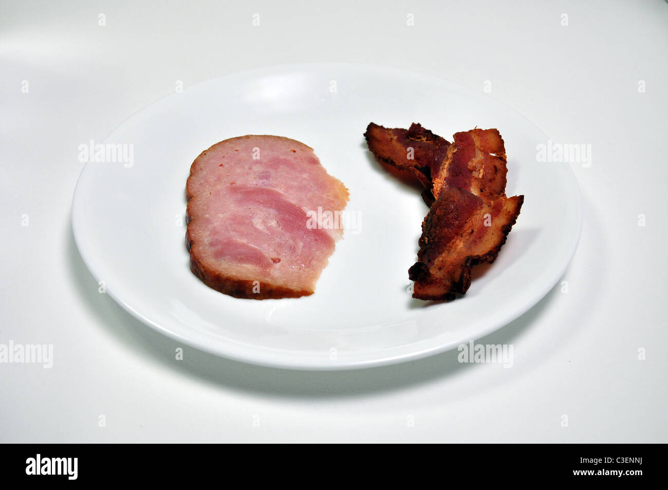 Eine Scheibe Schinken ist auf einem Teller mit einer Scheibe Speck. Stockfoto