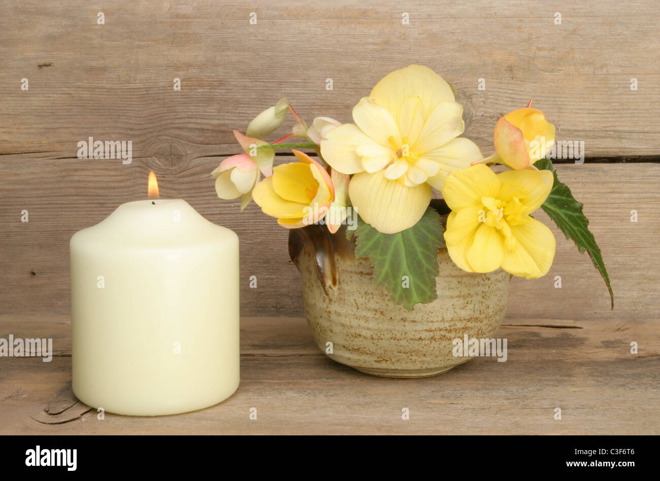 Anordnung der gelbe Begonie Blumen und eine brennende Kerze auf einem Hintergrund von verwittertem Holz Stockfoto