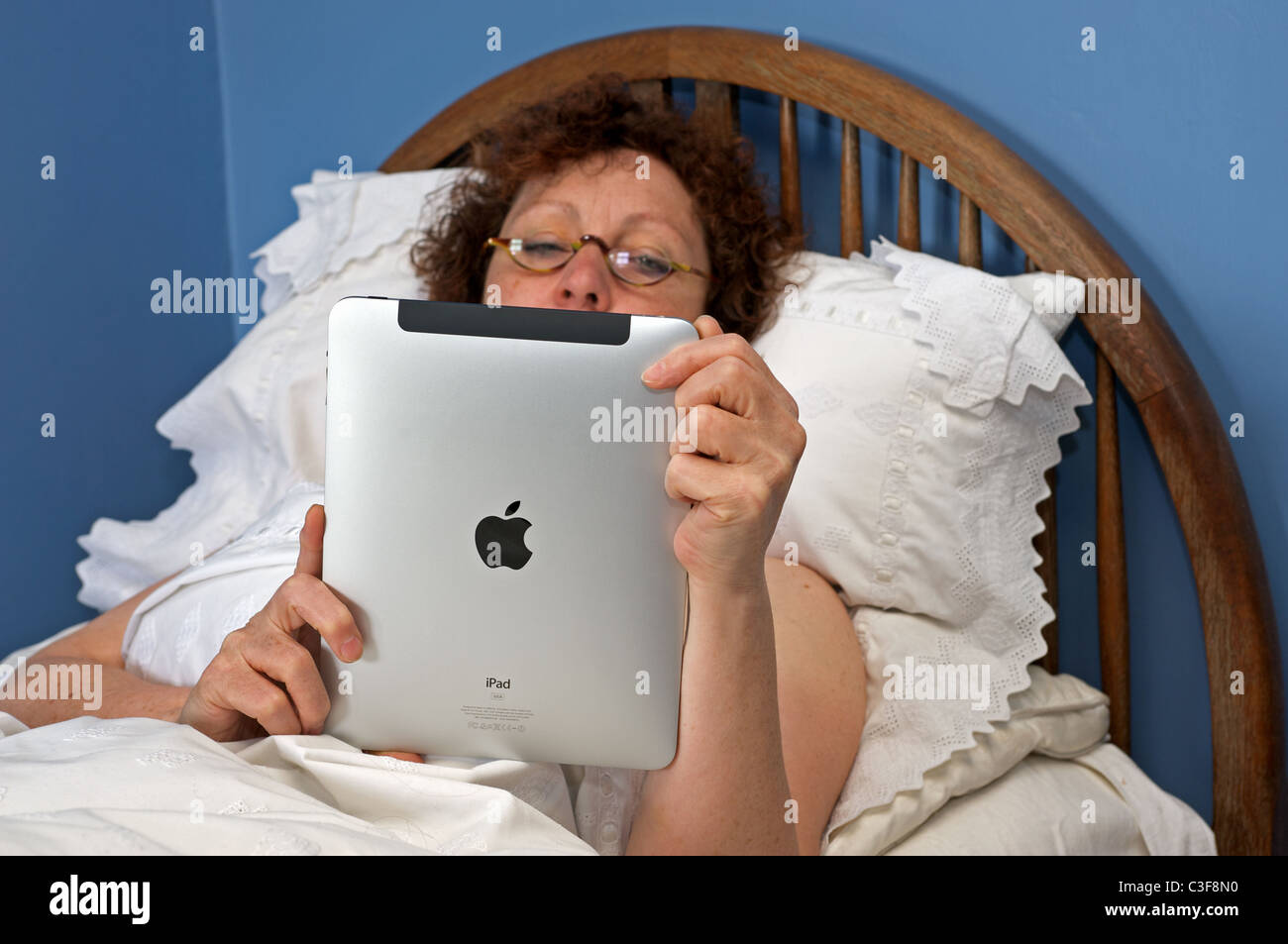 Frau im Bett und las ein Buch über ein Apple iPad Tablet-computer Stockfoto