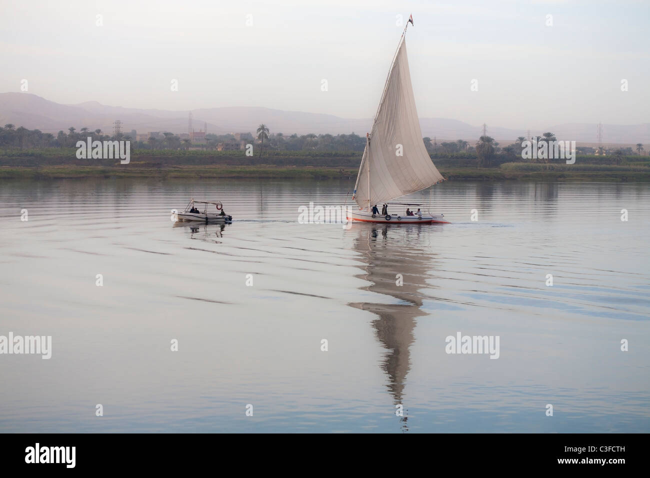 Feluke abgeschleppt mit dem Motorboot auf dem Nil bei Sonnenuntergang, Luxor, Ägypten, Nordafrika Stockfoto