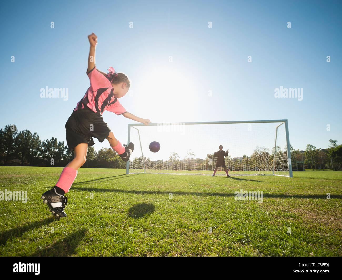 Mädchen-Fußball-Spieler treten Fußball am Netz Stockfoto