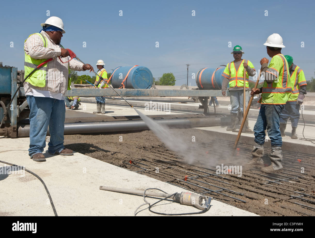 Hispanische männlichen Autobahn Arbeiter Sprays Wasser über frisch gegossenem Beton auf die richtige Temperatur zu gewährleisten Stockfoto