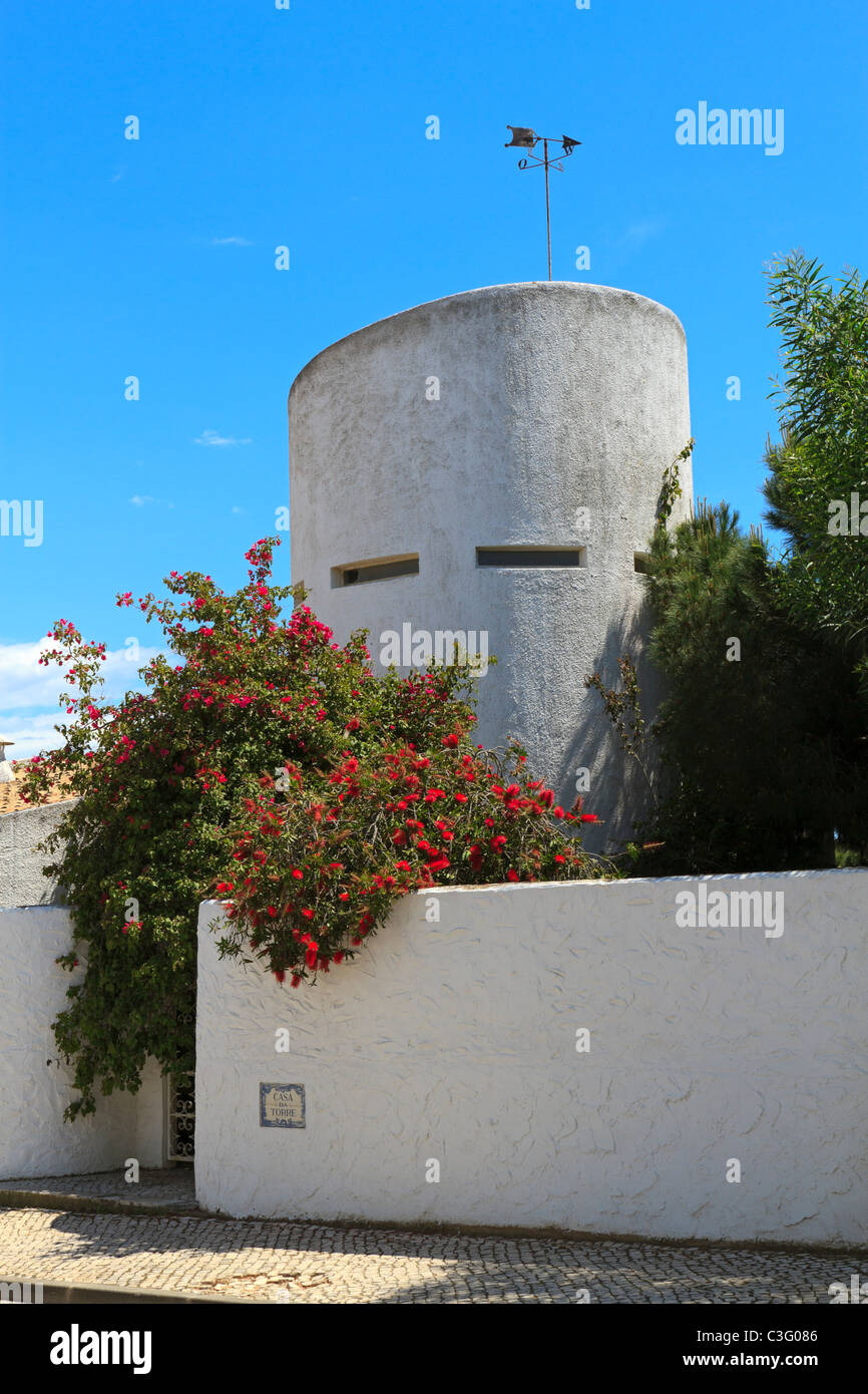 Haus in Albufeira, Portugal. Ein Turm mit kleinen Fensteröffnungen erhebt sich über die Gartenmauer eines Hauses an der Algarve. Stockfoto