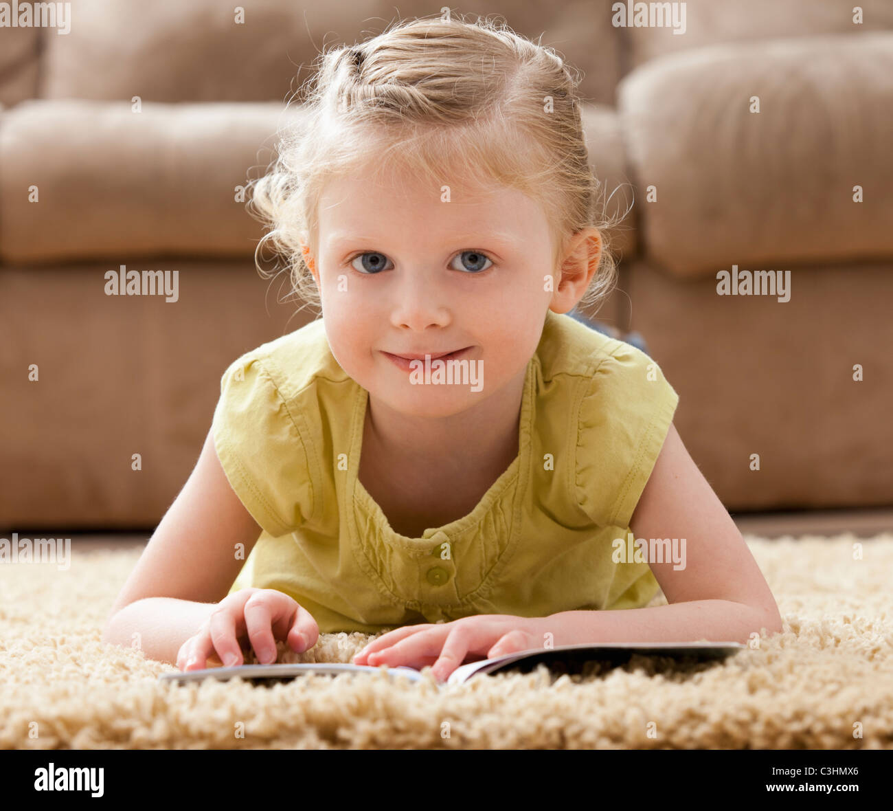Porträt von lächelndes Mädchen (2-3) auf Teppich liegend mit Buch Stockfoto