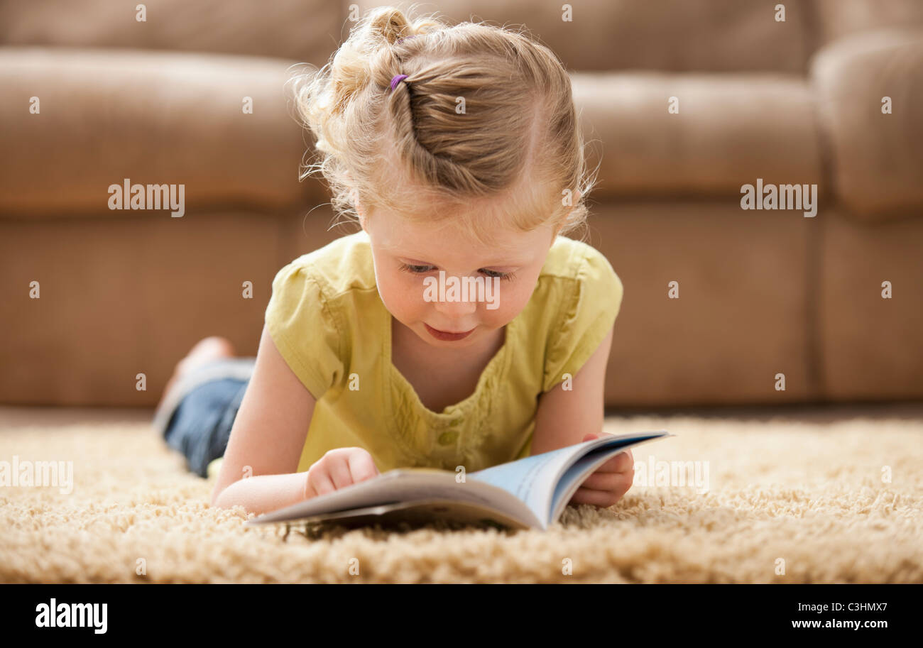 Mädchen (2-3) liegen auf Teppich, Buch lesen Stockfoto