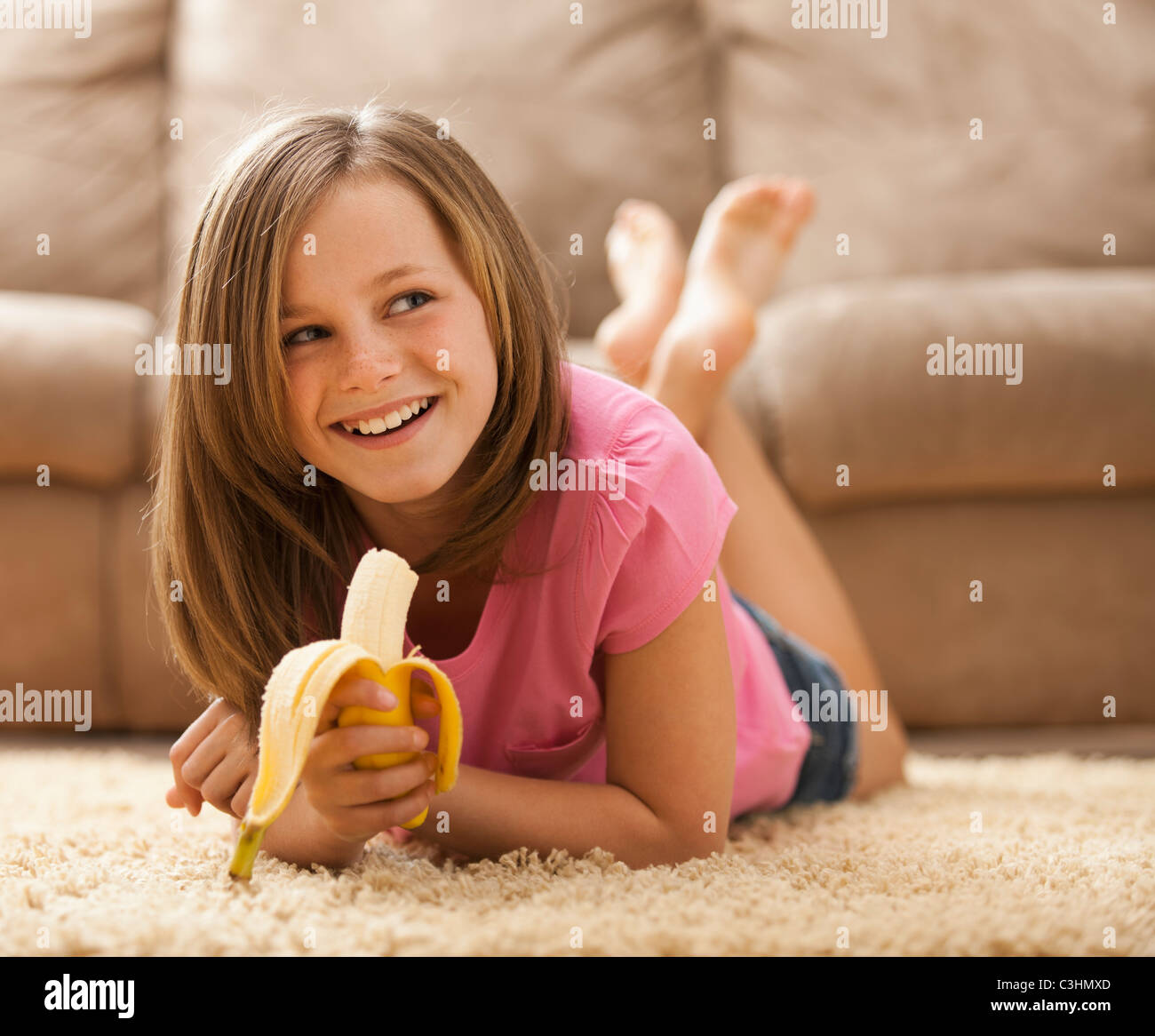 Mädchen (10-11) liegen auf Teppich, Banane essen Stockfoto