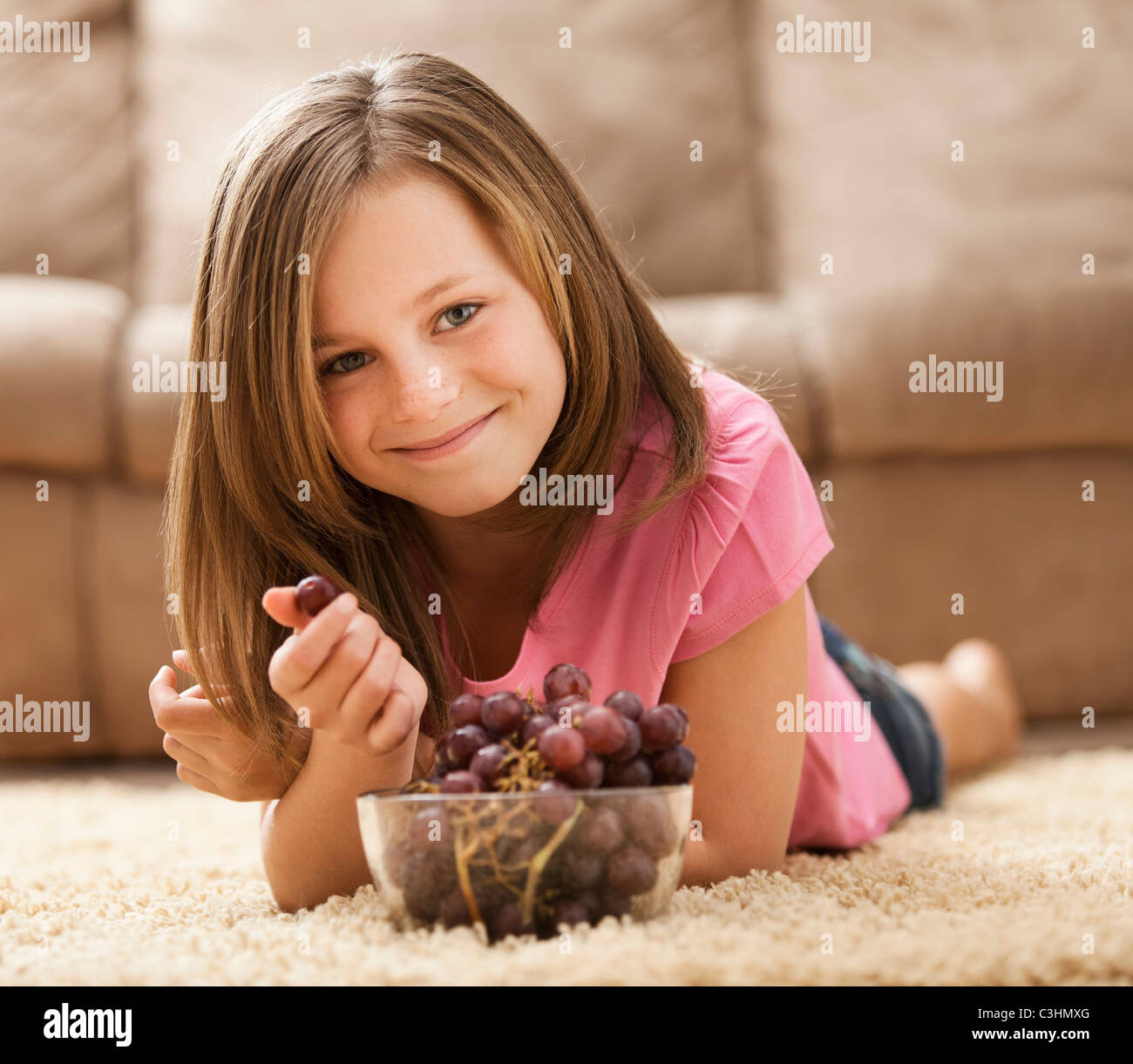 Porträt von Mädchen (10-11) liegen auf Teppich, rote Trauben essen Stockfoto