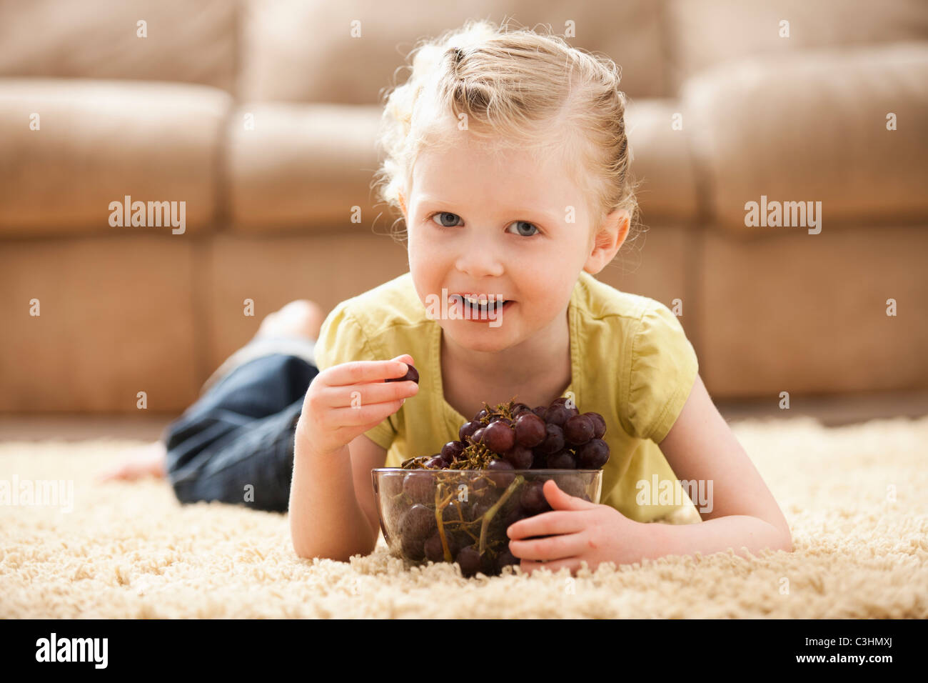 Mädchen (2-3) auf Boden essen Trauben Stockfoto
