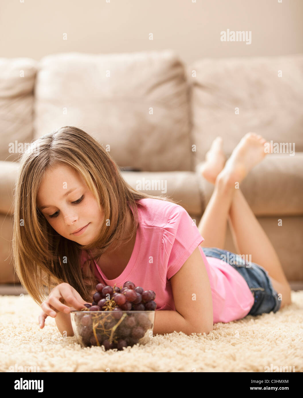 Mädchen (10-11) auf Boden essen Trauben Stockfoto