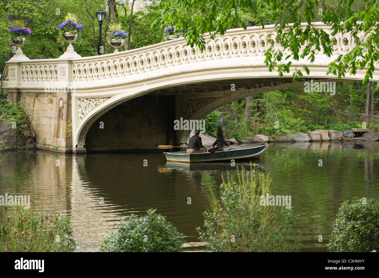 Zwei Personen in einem Ruderboot unter Bogenbrücke im New Yorker Central Park mit Blick auf die Wanderung. Stockfoto