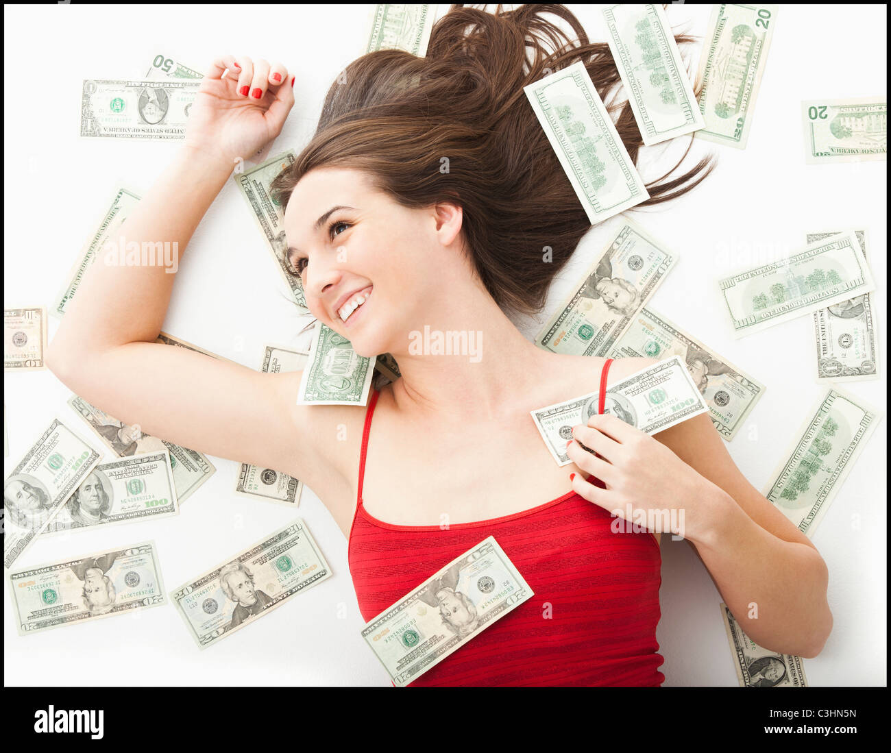 Junge Frau, die in Geld liegen Stockfoto