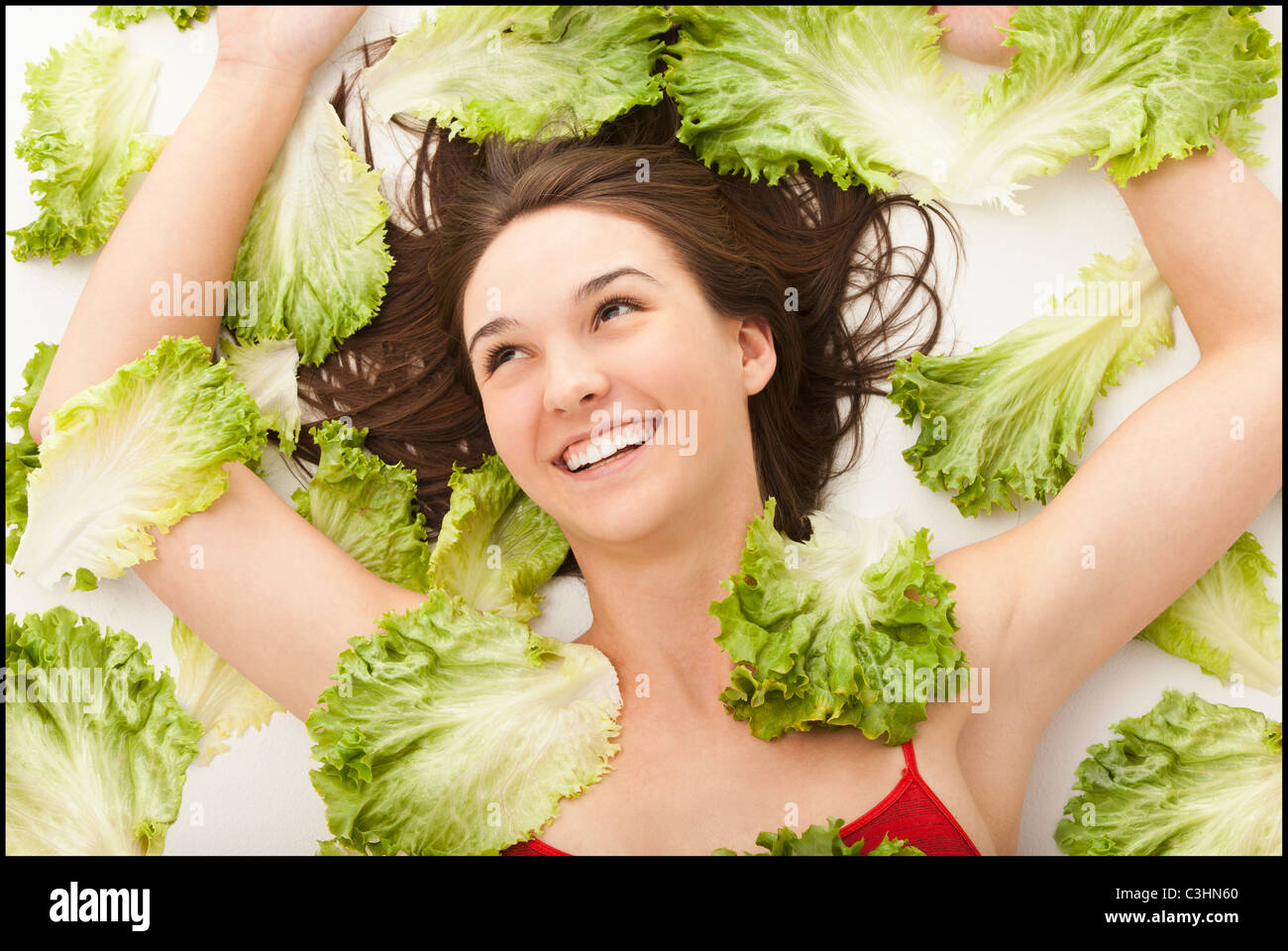 Junge Frau in Salatblätter liegen Stockfoto