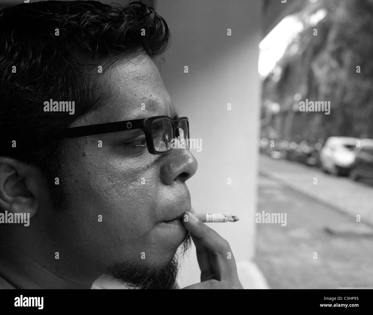 Seitenansicht einer südasiatischen Youngster Rauchen Zigarette Spektakel Brille Brille specs Gläser Tabak b&w Stockfoto