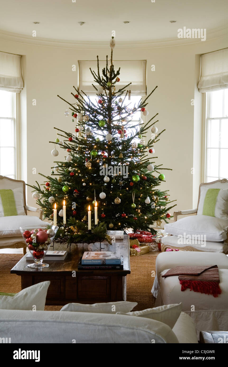 Geschmückter Weihnachtsbaum mit Kugeln im regency Wohnzimmer mit Sesseln und Kerzen Stockfoto