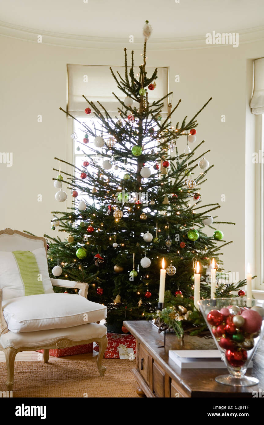 Geschmückter Weihnachtsbaum mit Kugeln im Wohnzimmer mit Sessel und Kerzen Stockfoto