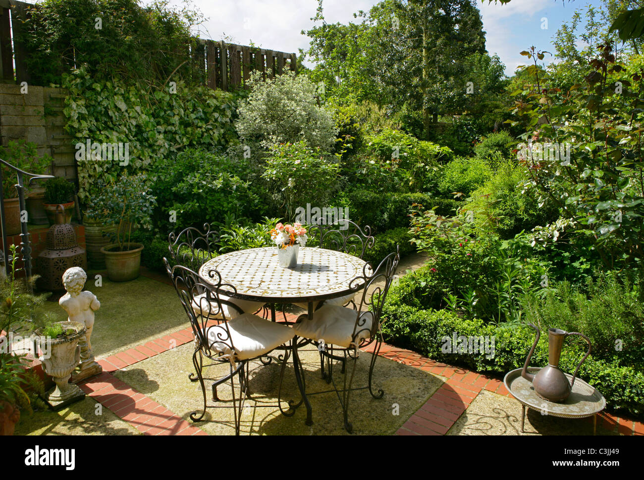 Kleinstadt Gartenterrasse mit Möbel aus Metall und gefliesten Tisch Sträucher und Feld hedge Stockfoto