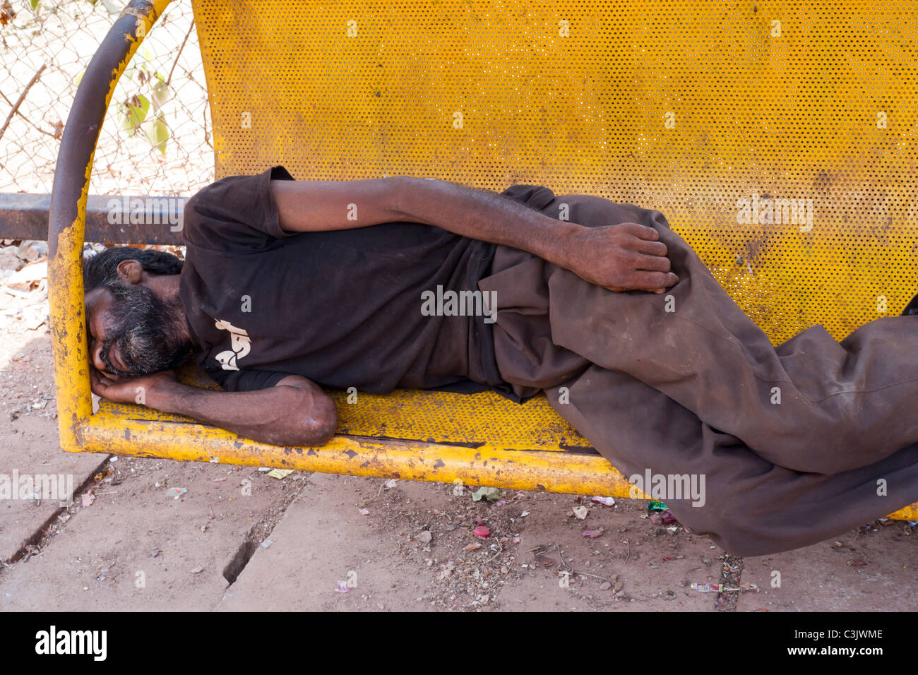 Down and out in Goa. Eine asiatische Bettler an einer Bushaltestelle in Calangute Hautpstraße, Goa eingeschlafen. Stockfoto