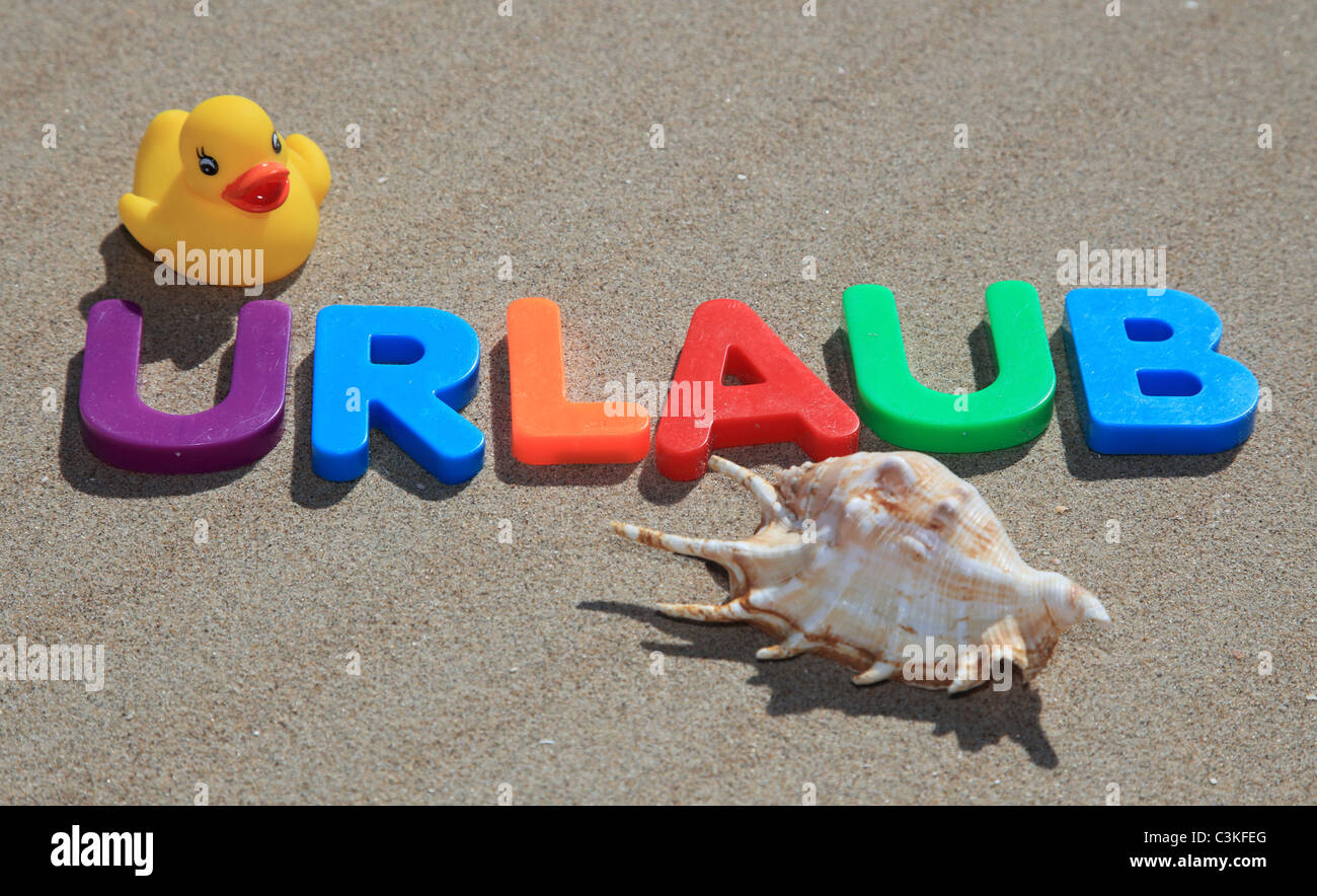 Der deutsche Begriff Urlaub (engl.: Urlaub) auf dem Sand in bunten Lettern geschrieben. Stockfoto