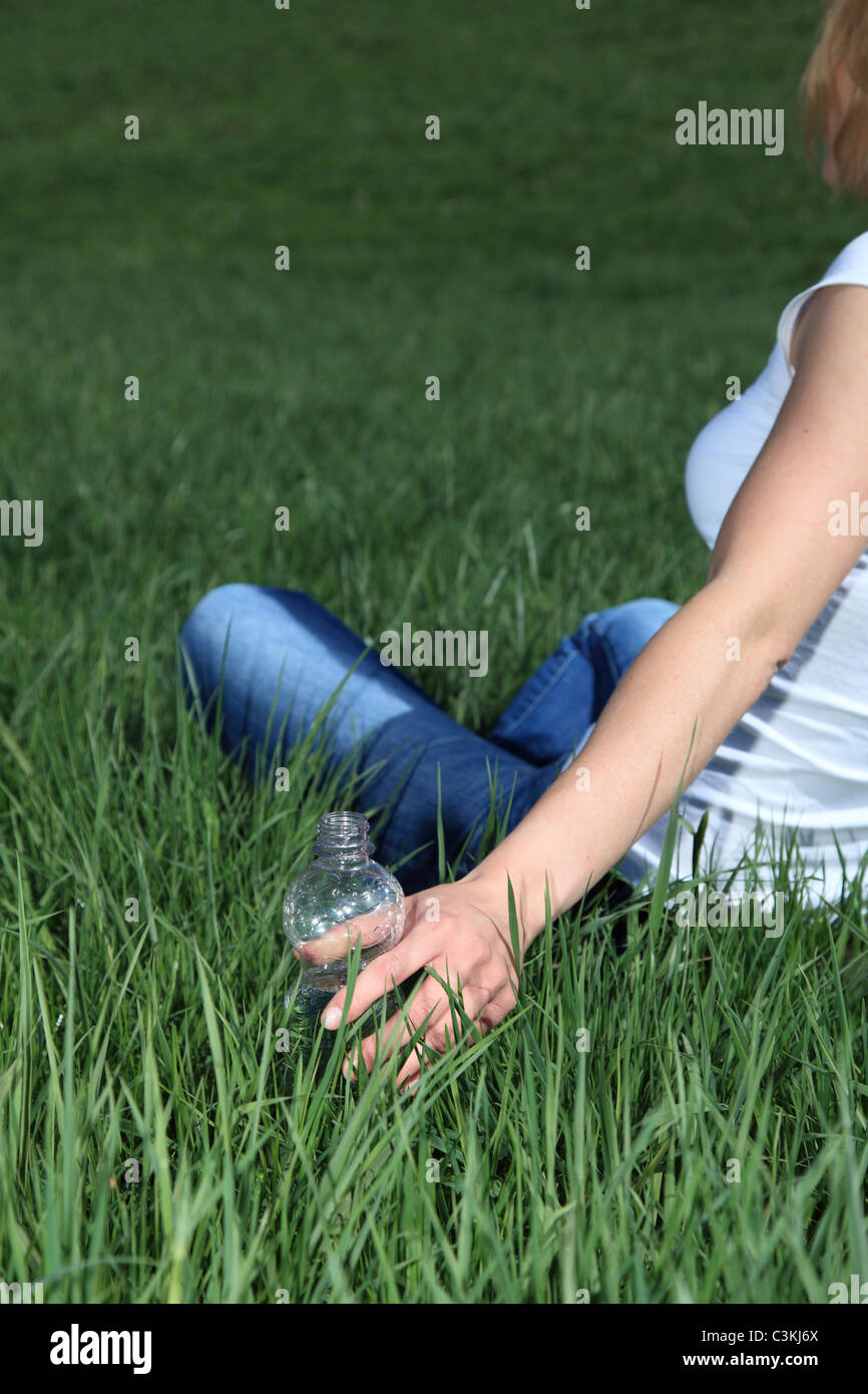 Junge Frau für eine Flasche Wasser zu erreichen, während draußen zu sitzen Stockfoto