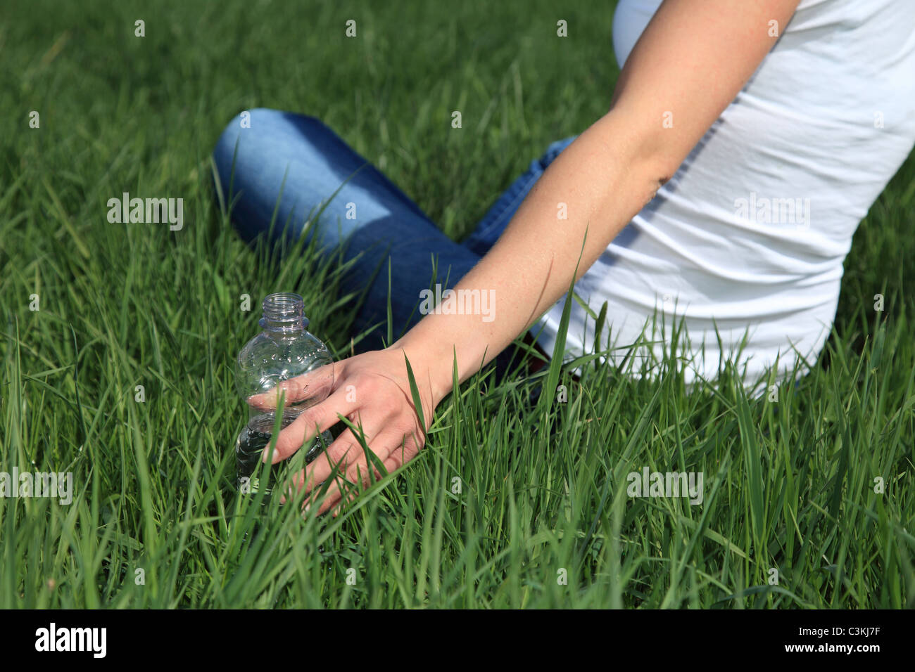 Junge Frau für eine Flasche Wasser zu erreichen, während draußen zu sitzen Stockfoto