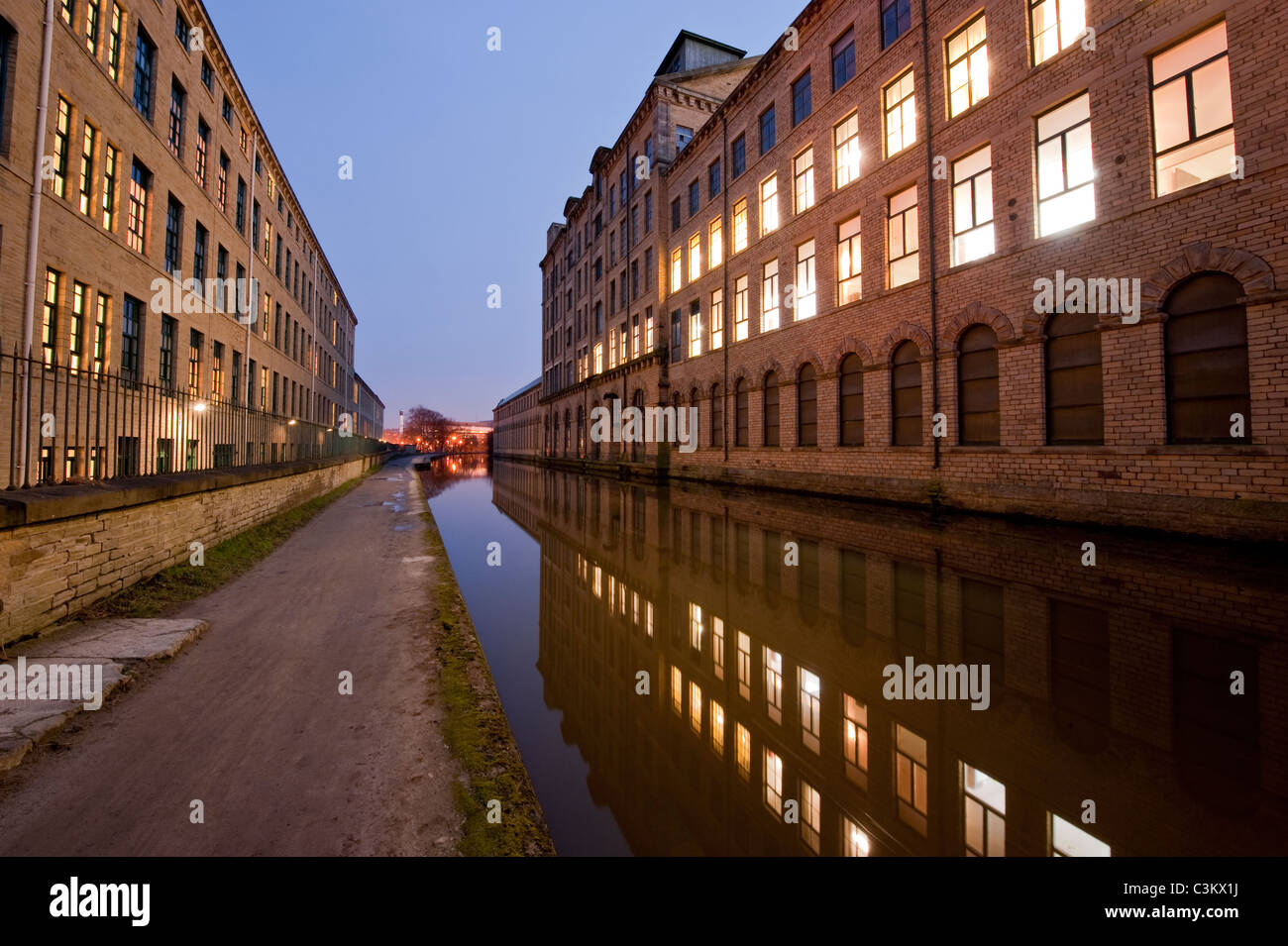 Salts Mill in Evening (historisches viktorianisches Textilmühlengebäude, Lichter an, Reflexion auf Kanalwasser) - Leeds Liverpool Canal, Saltaire, England, Großbritannien. Stockfoto