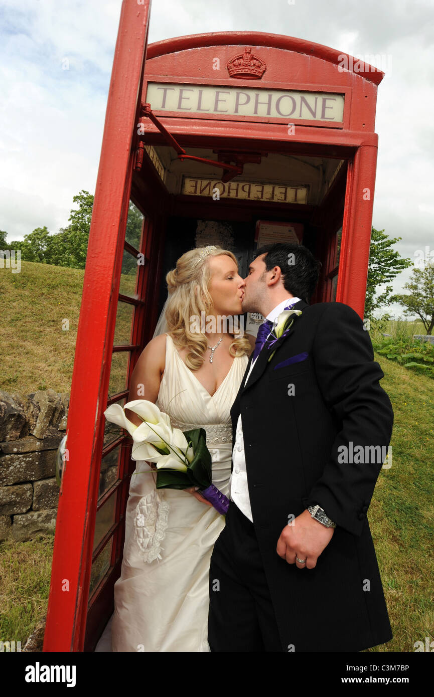 Britische traditionelle Braut und Bräutigam küssen in eine traditionelle rote Telefonzelle am Tag ihrer Hochzeit Stockfoto