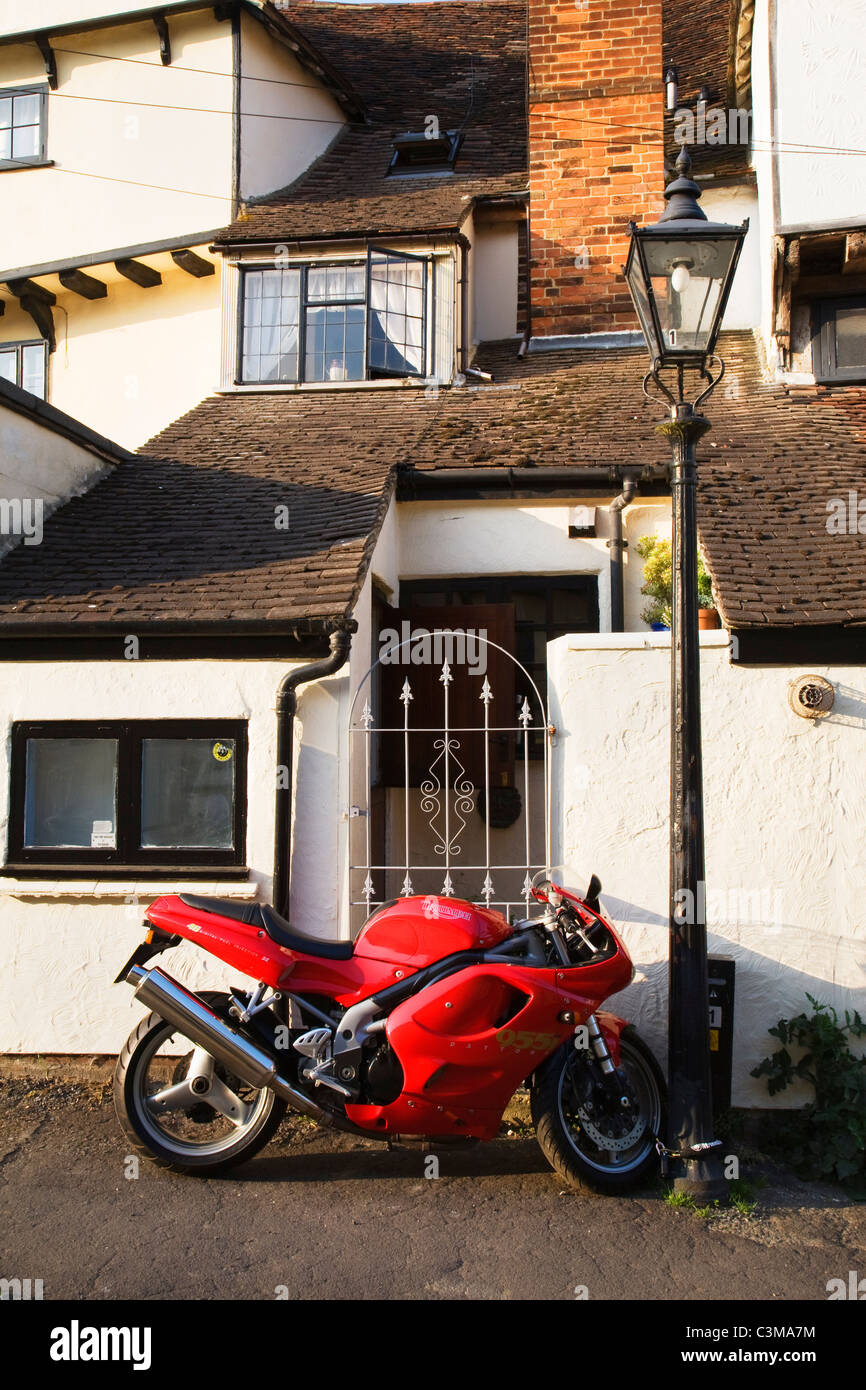 Ein leuchtend rotes Motorrad steht außerhalb der malerischen Häuser in der historischen Stadt Thaxted in Essex. Stockfoto