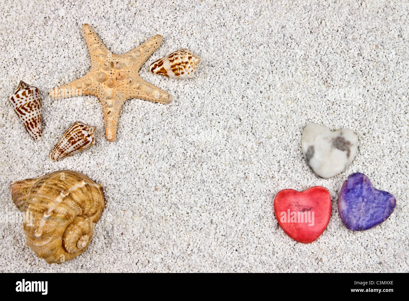 ein Seastar und mehrere Muscheln im weißen Sand mit drei Herzen Stockfoto