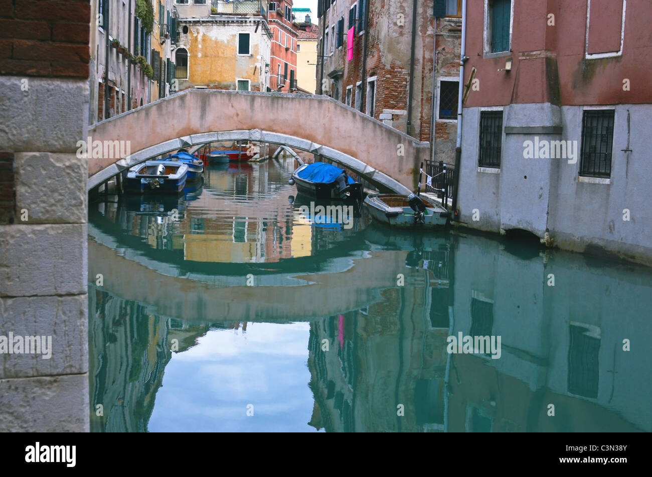 Ein Rückstau in Venedig auf der Suche an einem Kanal in Richtung einer Brücke mit Häuser entweder Seite & die Szene im Wasser reflektiert wird. Stockfoto