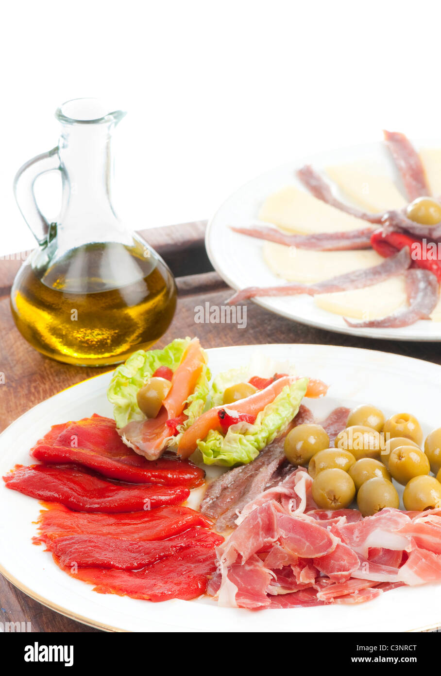 Spanische Tapas mit Olivenöl, Serrano-Schinken, Käse, gebratene Piquillo Paprika, Oliven, Sardellen und Salat auf einem Holzbrett. Stockfoto