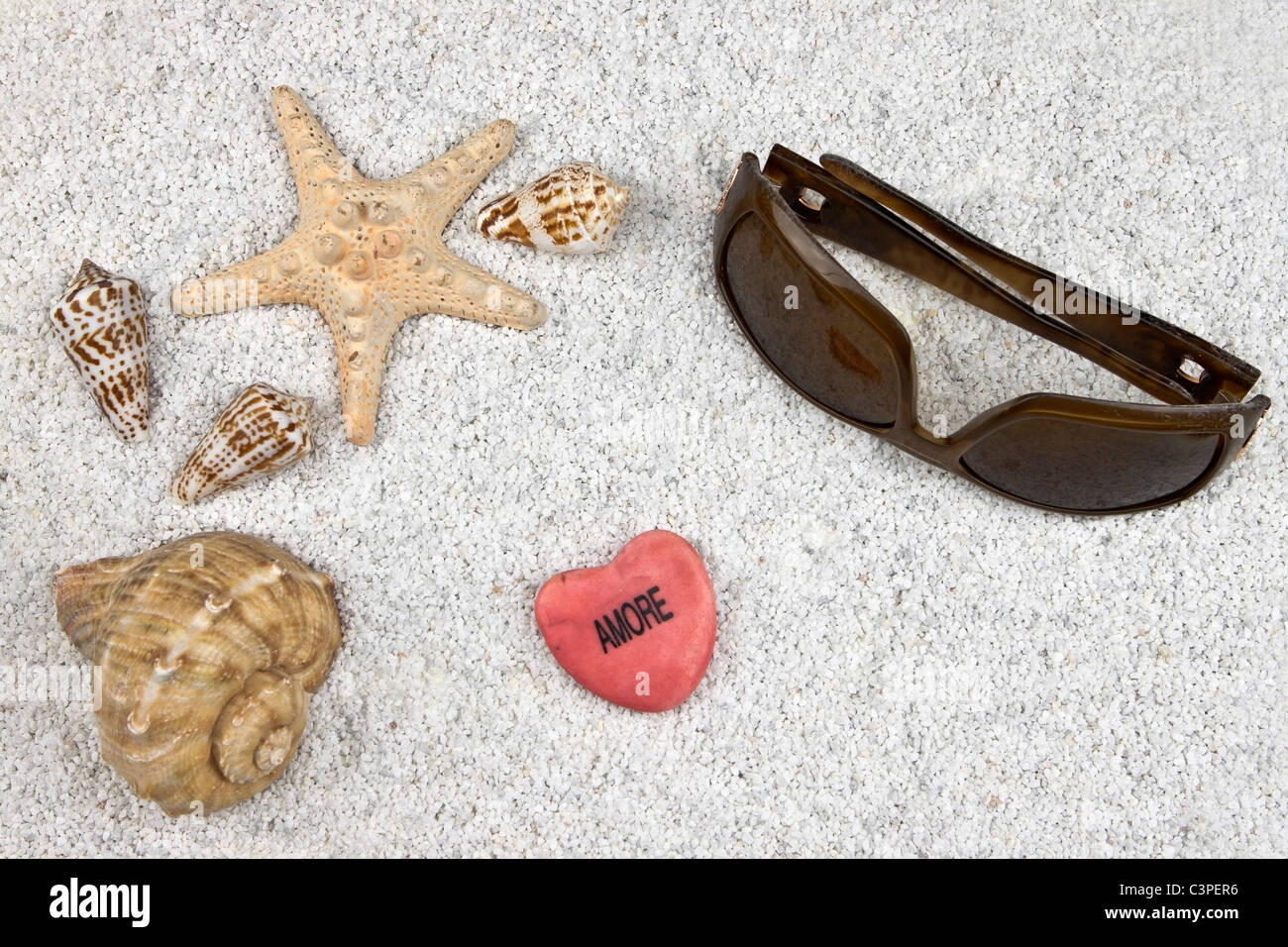 ein Seastar und mehrere Muscheln im weißen Sand mit Sonnenbrille und ein Herz Stockfoto