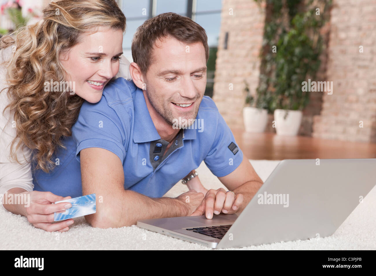 Deutschland, Köln, paar liegen auf Teppich mit Laptop, Porträt Stockfoto