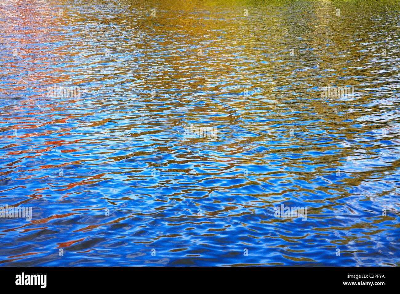 Die Oberfläche eines kleinen Sees spiegelt die leuchtenden Farben der umgebenden Herbstlaub und der tiefblaue Himmel Stockfoto