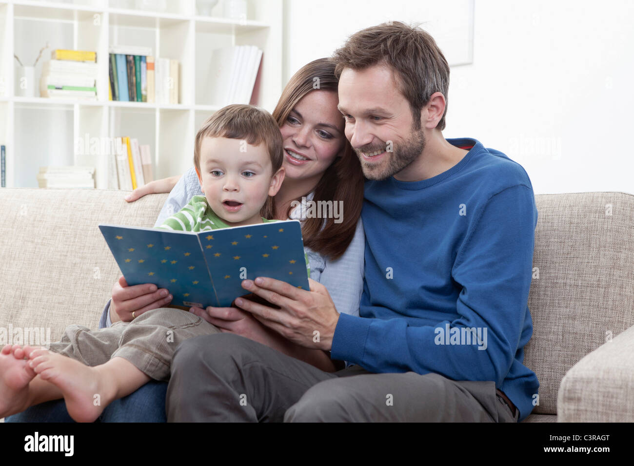 Deutschland, Bayern, München, Eltern Buch mit Sohn (2-3 Jahre) im Wohnzimmer Stockfoto