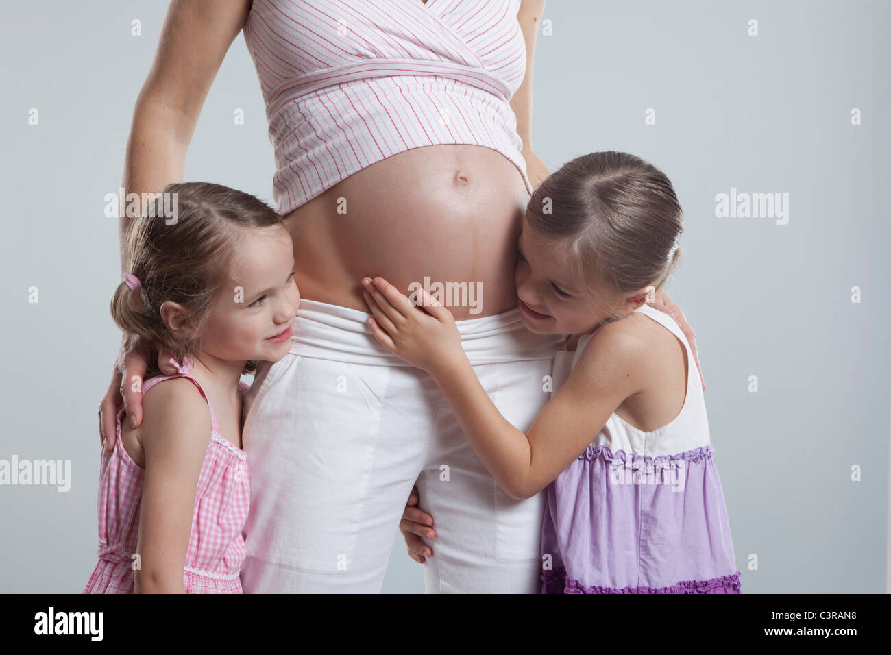 Töchter, die schwangere Mutter umarmen Stockfoto