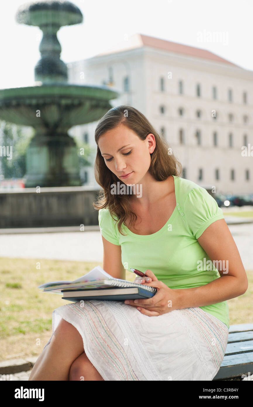 Deutschland, München, junge Frau auf der Bank sitzen und lesen Stockfoto